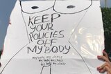 A protester holds a sign reading' 'Keep your policies off my body' and 'My body my choice'.
