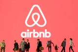 Small toy figures are seen in front of diplayed Airbnb logo.