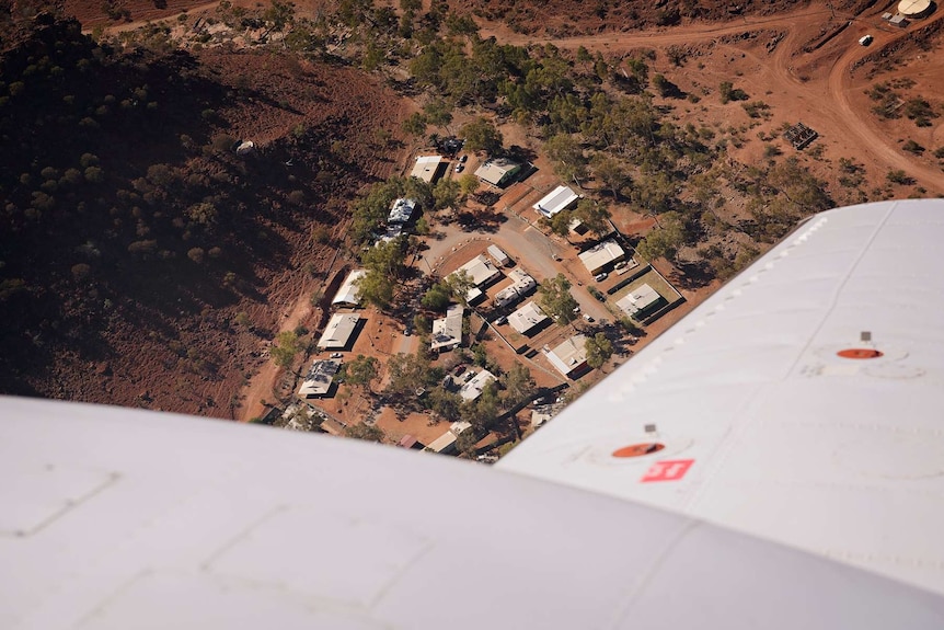 An aerial shot of Areyonga community shows buildings on the ground with a plane wing in the foreground.