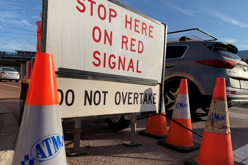 A 'stop here on red signal' road sign and orange cones with the Australian Traffic Management logo, with a car nearby.