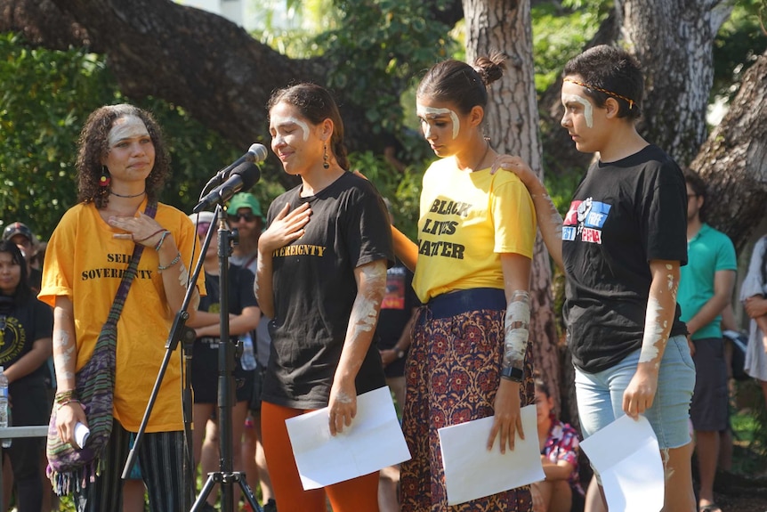 Four women have their hands on each other and are standing in front of the microphone