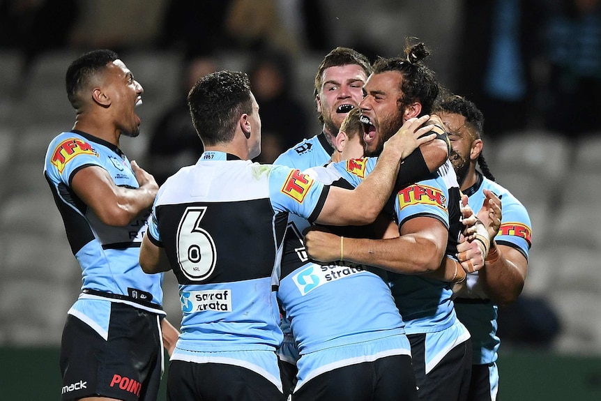 Cronulla NRL players embrace one of their teammates after he scored a try against the Warriors.