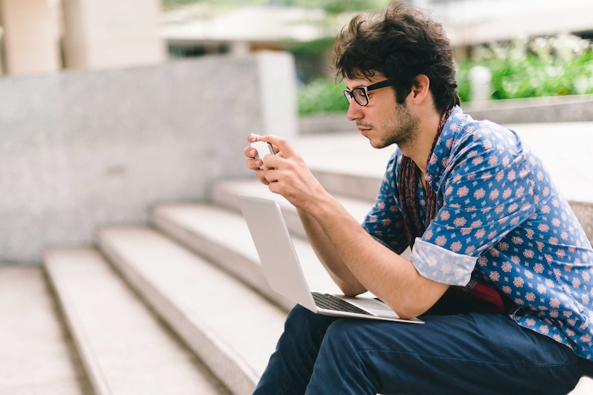 Male student looking at phone and laptop