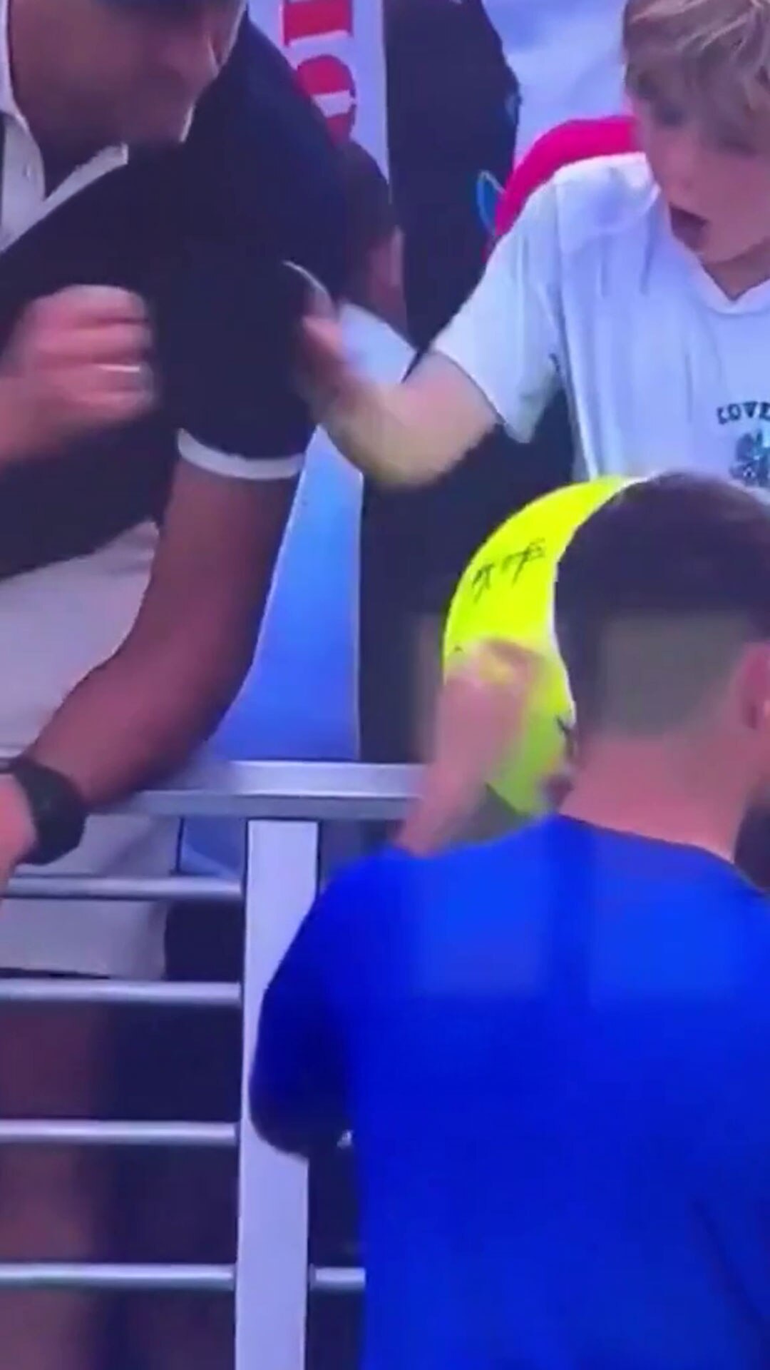 A tight shot shows a man and a boy in grandstand seating holding a cap, the boy looks surprised.