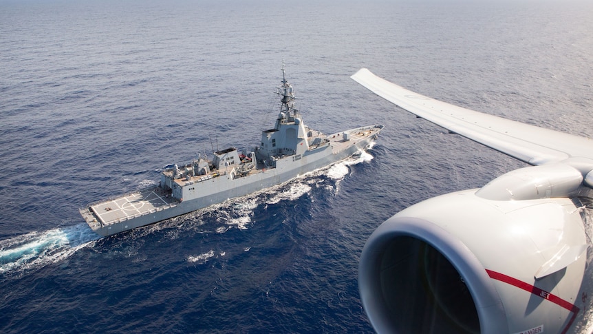 A jet engine is seen overhead of a large ship on open waters