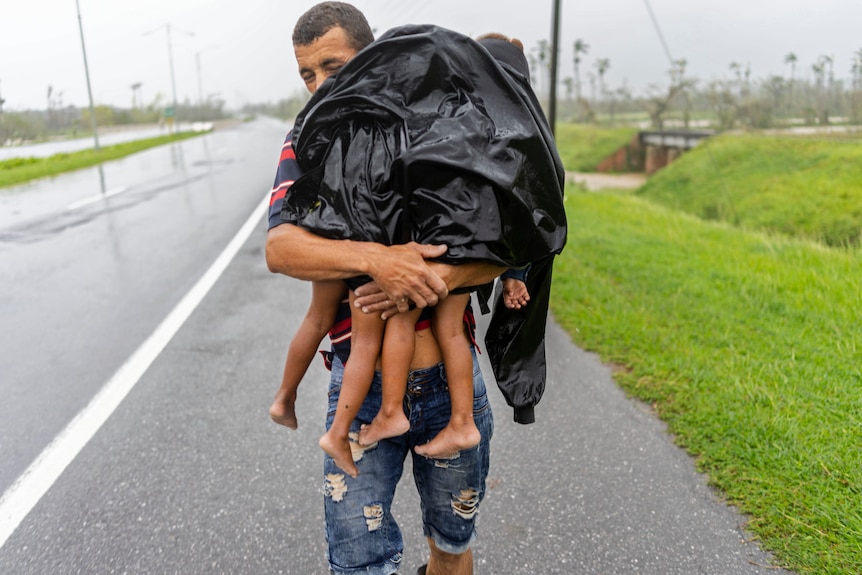 Un hombre que lleva niños pequeños mostrando sus pies bajo una sábana de plástico negro cubierta por la lluvia