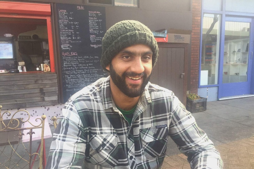 Ananth Gopal, wearing a beanie and flannelette, sits outside a cafe