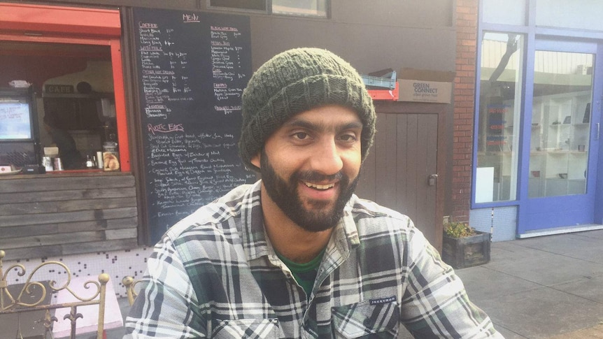 Ananth Gopal, wearing a beanie and flannelette, sits outside a cafe