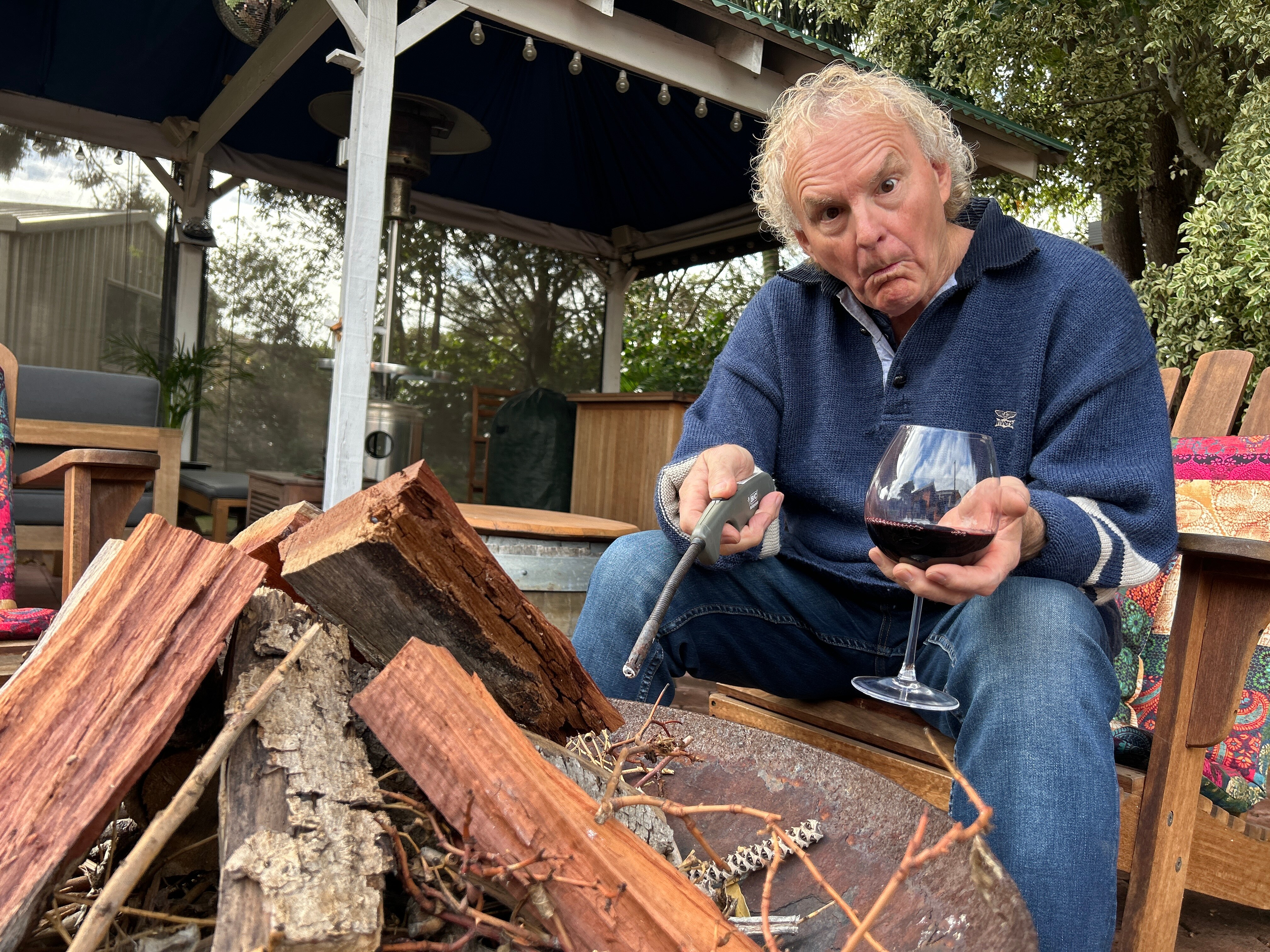 Man holding glass of wine and lighter in front of wood fire pit 