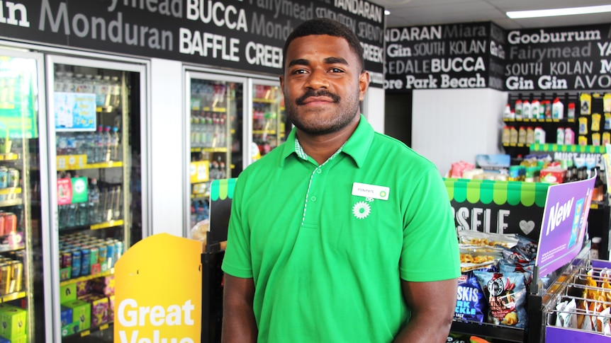 A service station employee wearing a green shirt stands in front of a shelf