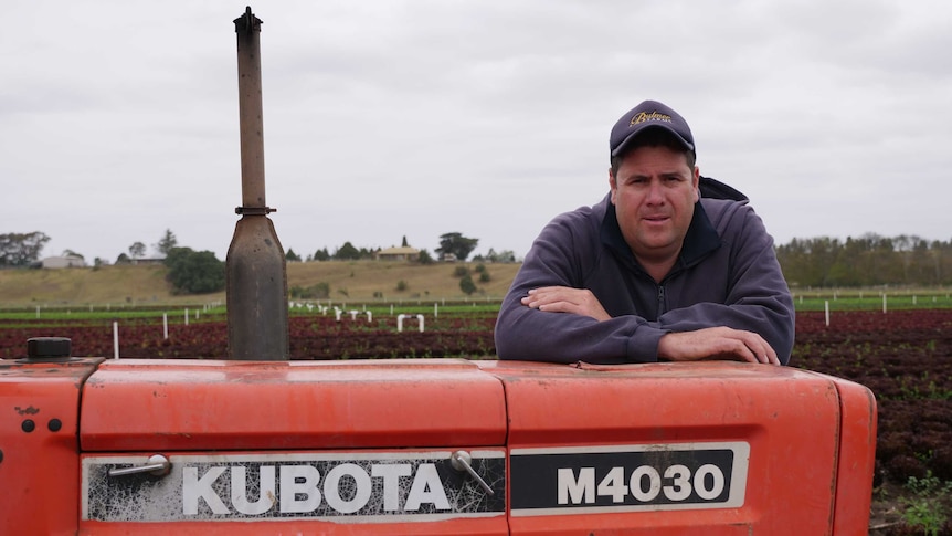 Veggie and salad farmer, Andrew Bulmer leans on his red tractor with a view of the field in the background.