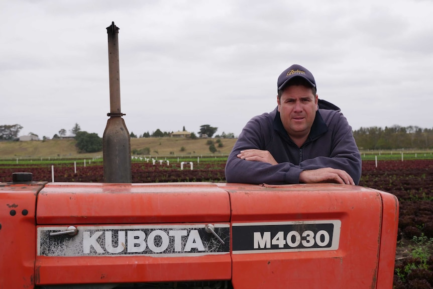 Veggie and salad farmer, Andrew Bulmer leans on his red tractor with a view of the field in the background.