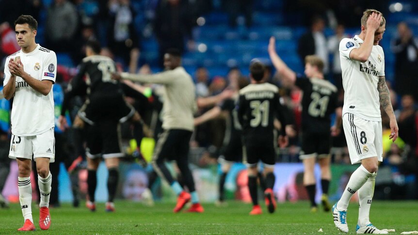 Two players look dejected after a Champions League tie, while the winners celebrate in background.