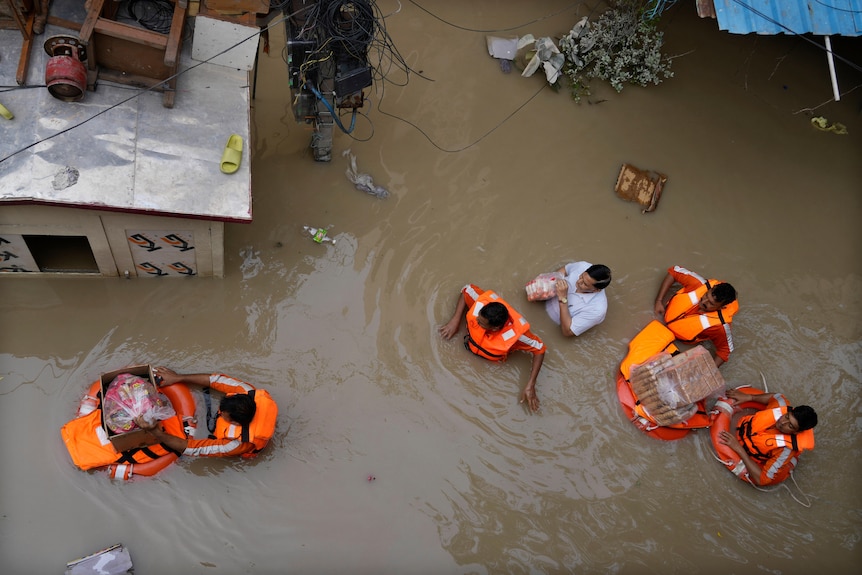 Работники по оказанию помощи доставляют гуманитарную помощь с помощью плавучих средств в паводковых водах.