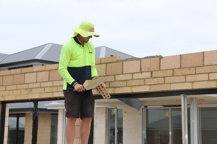 A bricklayer in high-vis gear lays bricks.