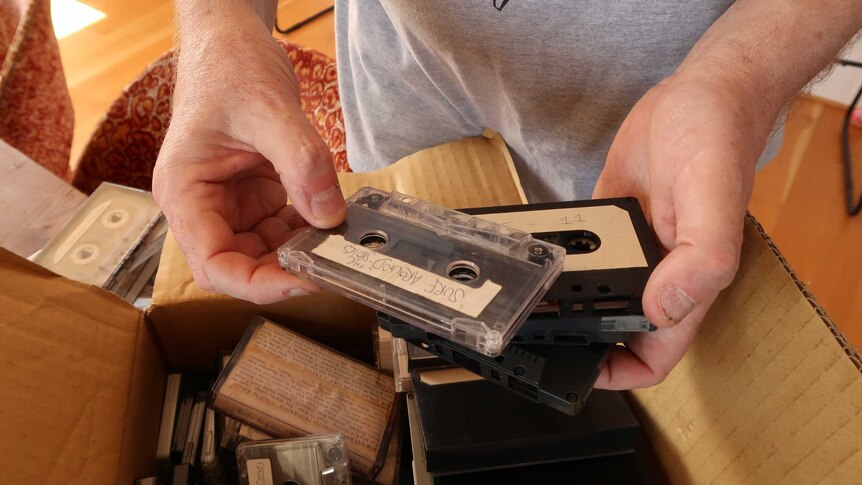 A man sorts through a box of old cassette tapes