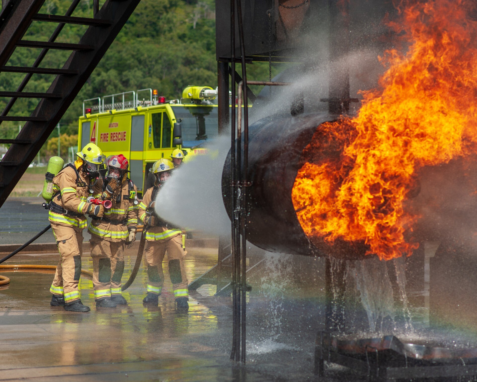 Firefighters aiming a huge torrent of water from a hose at a prop jet engine ablaze.