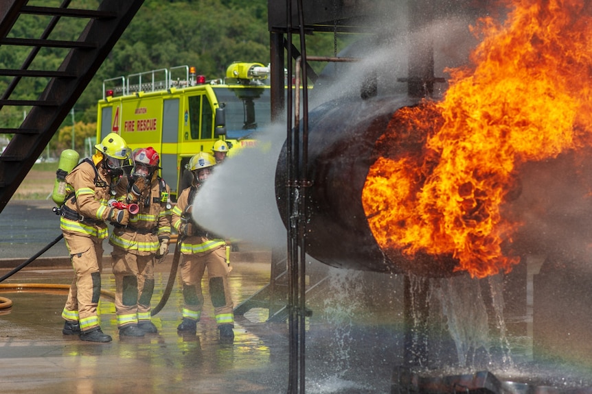 Firefighters aiming a huge torrent of water from a hose at a prop jet engine ablaze.