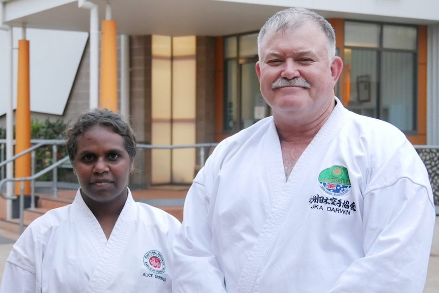 Indigenous teenager Chrissie Davis and her coach, Michael Schumacher, stand looking at the camera in karate gear.