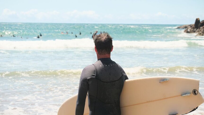 A man holding a surfboard looks out to sea.