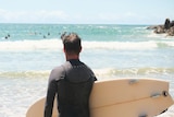 A man holding a surfboard looks out to sea.