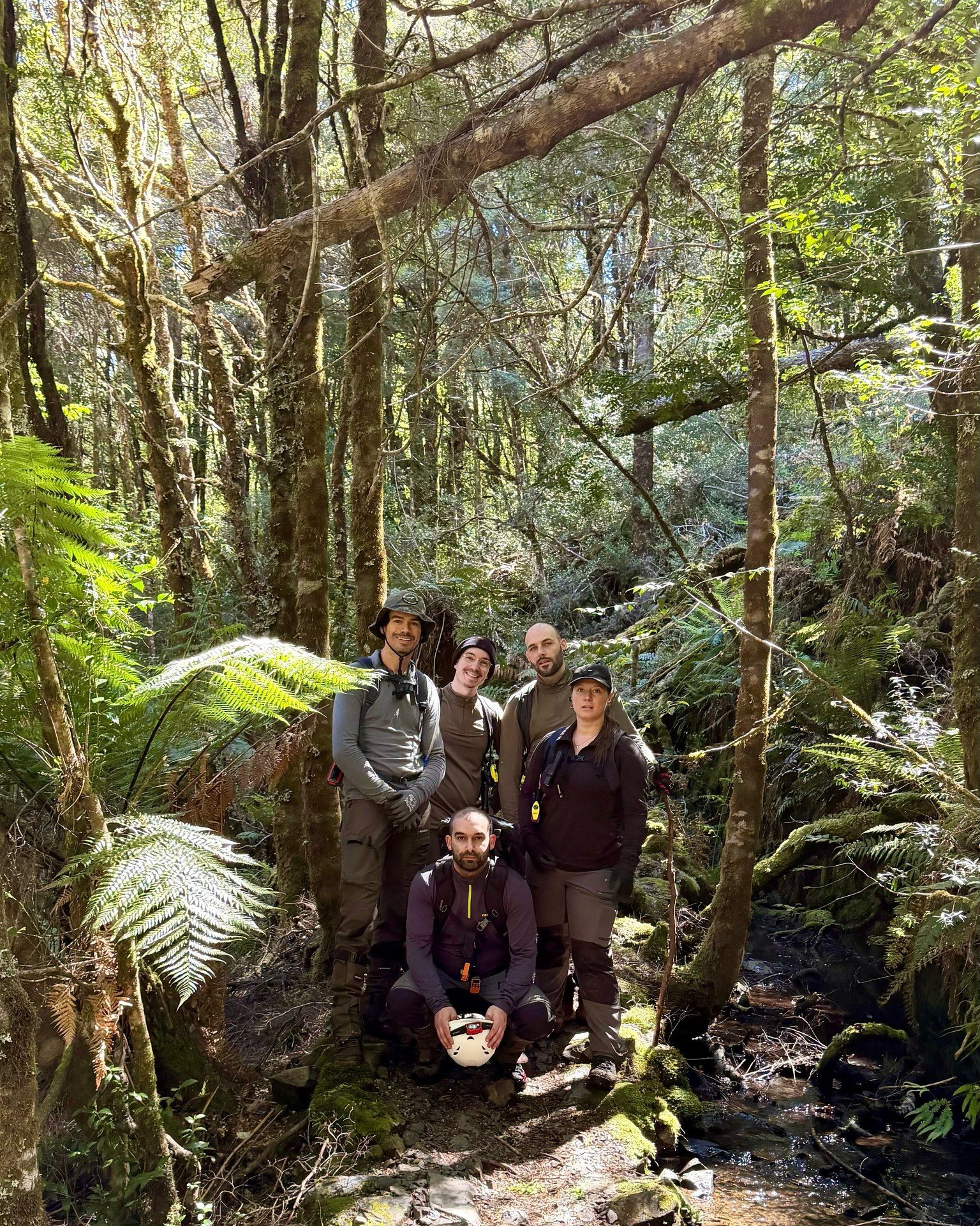 A group of five people standing in thick bushland, smiling at the camera.