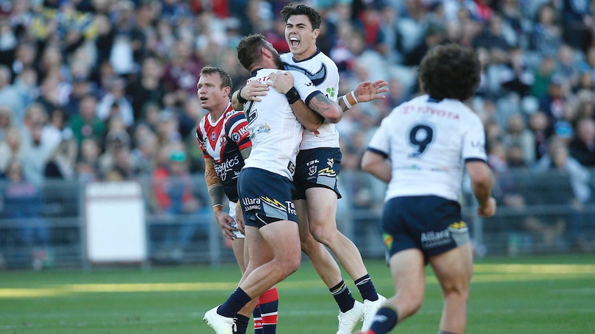 A male NRL player screams out as he jumps in the air while hugging a standing teammate after kicking a field goal.