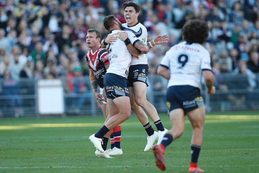 A male NRL player screams out as he jumps in the air while hugging a standing teammate after kicking a field goal.