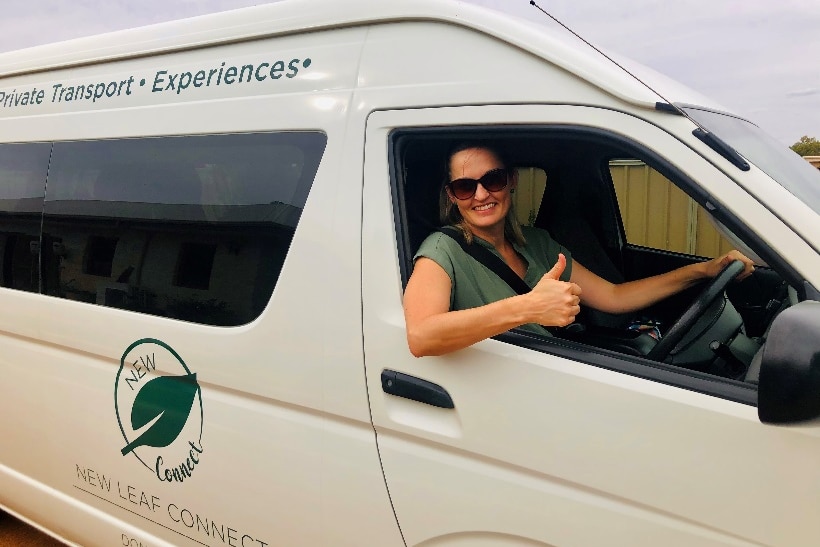 Front end of white van with lady in diving seat, holding thumbs up out window and smiling