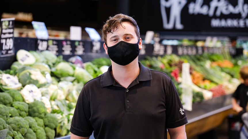 A man in a black face mask stands in the fruit and veg section of a supermarket.