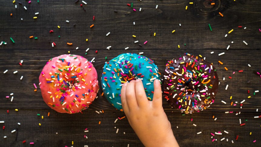 a child's hand reaches for brightly coloured doughnuts