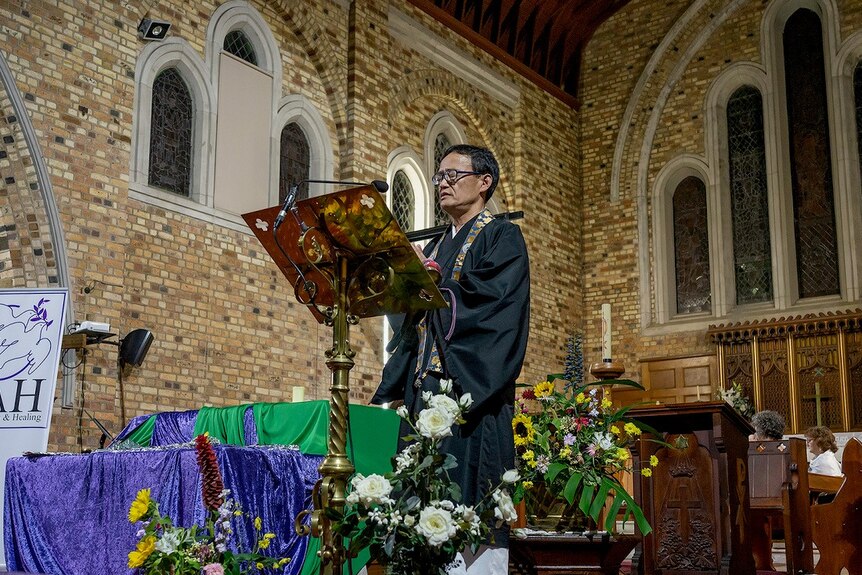 Buddhist reverend Shigenobu Watanabe speaking from a lectern in a church.