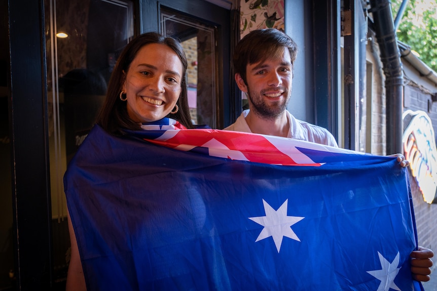 A young woman and man hold up an Australia flag.