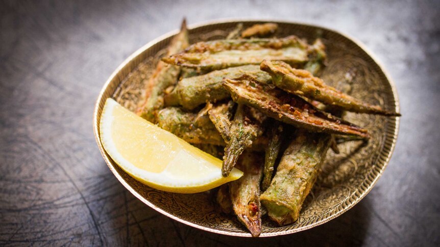 Fried okra with a wedge of lemon in a small bowl on slate bench.