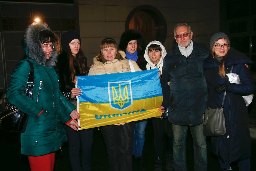 A group of seven people stand holding a Ukraine flag.