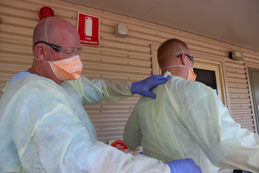 Two health workers in full PPE check each other's gowns.