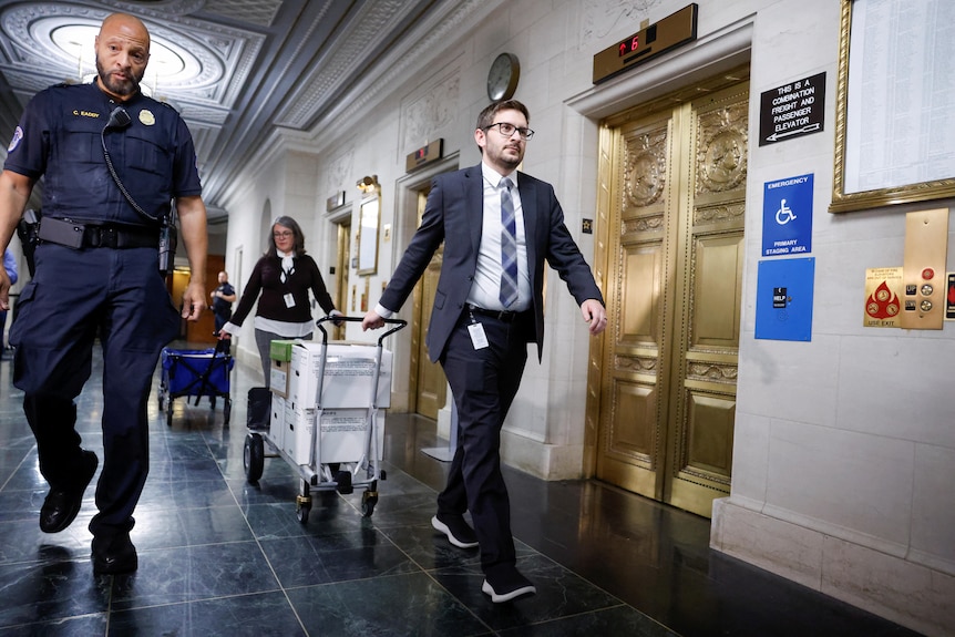 A man in a suit pulls a trolley stacked with boxes of documents past a golden door in US Congress
