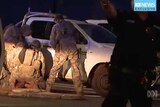 Three officials crouch over suspected gunman in Darwin. They wear camouflage gear and a white ute is behind them.