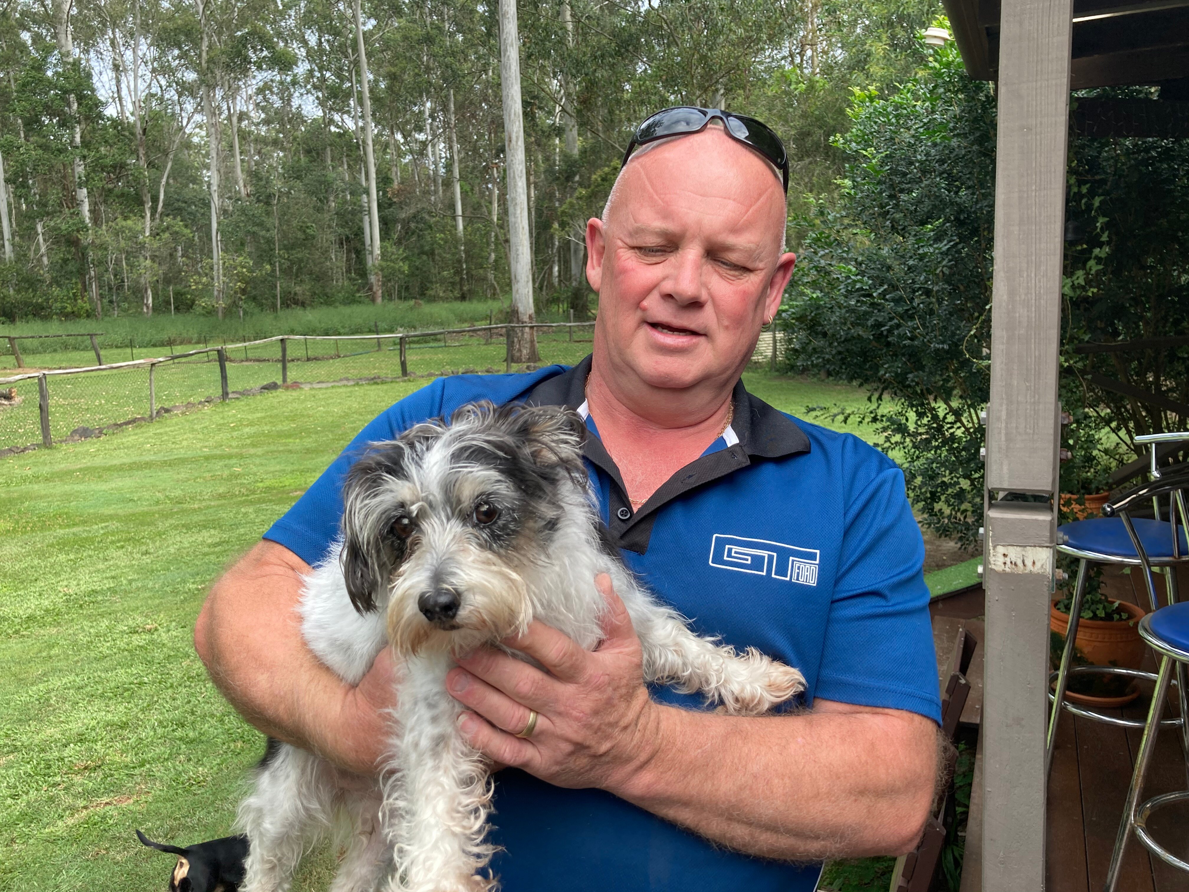 A smiling man holds a small grey and white dog.