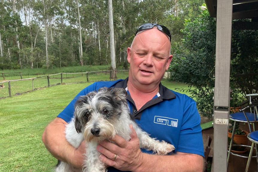 A smiling man holds a small grey and white dog.