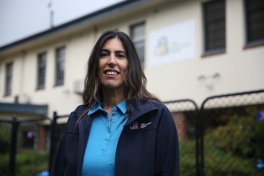 A woman with long brown hair smiles outside on a grey day.