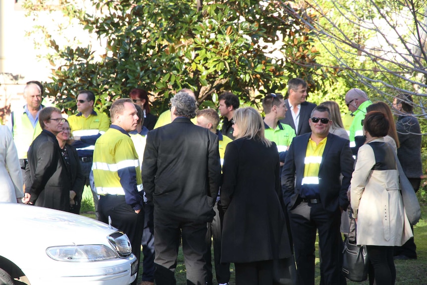 Workers in high-visibility gear stand near a tree outside a church.