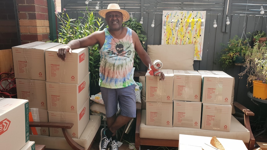 A man leans on piles of packed boxes stacked in a driveway.