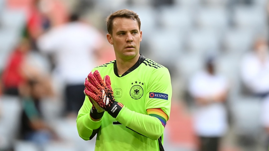 The German goalkeeper claps his hands on the pitch while wearing a rainbow armband supporting diversity and LGBTQ people.