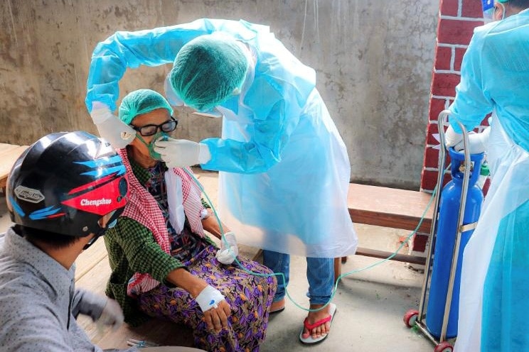 A volunteer in blue PPE puts an oxygen mask on a person.