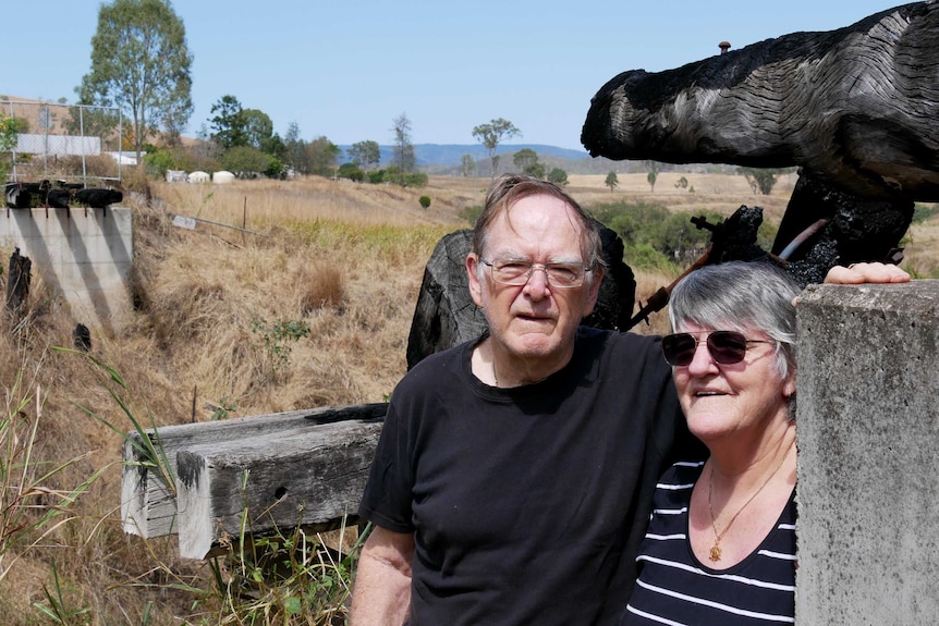 A man and woman stand under the charred remains of an old rail bridge on a rural property.