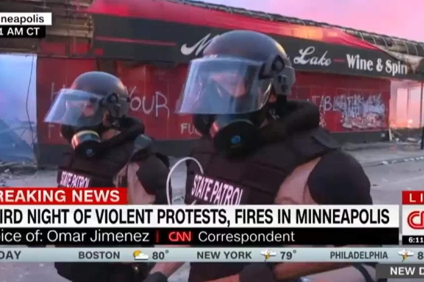 Police in gas masks stand around a television crew live on air during the Minneapolis riots