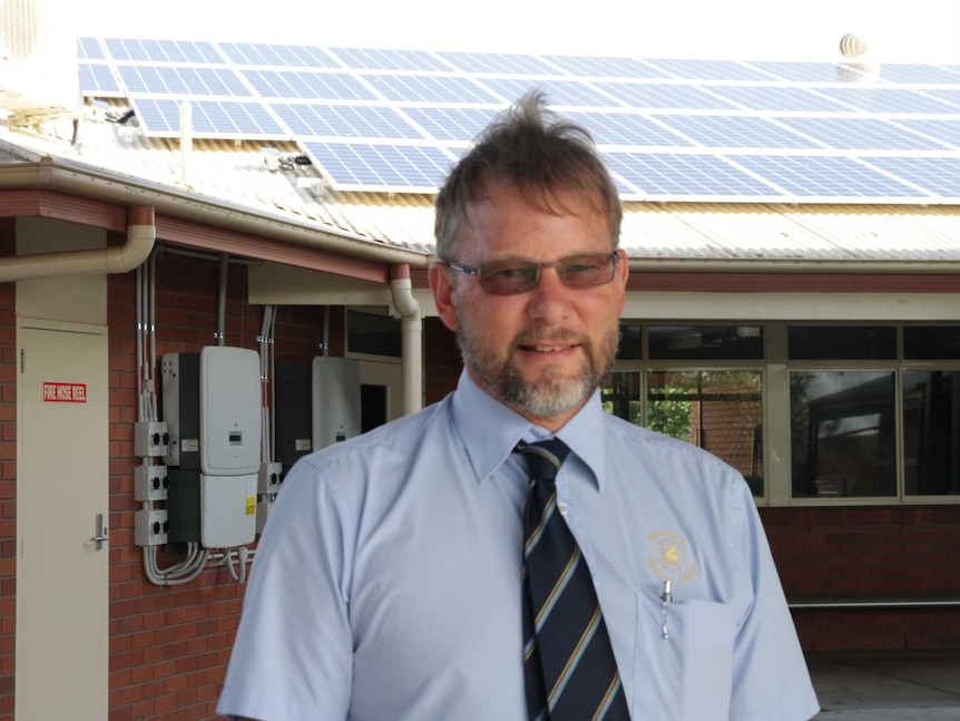 Bundaberg Christian College business manager Evan Keune in front of a school building with solar panels behind him.