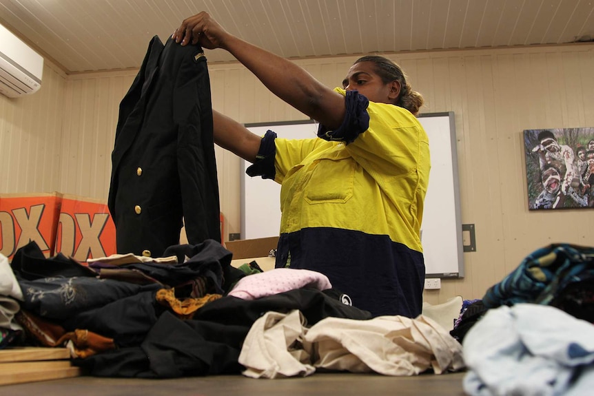 A photo of a Jilkminggan op shop employee unpacking a box of donated clothing.