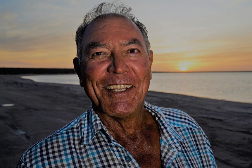 A close up of a man smiling while the sun sets behind him. 